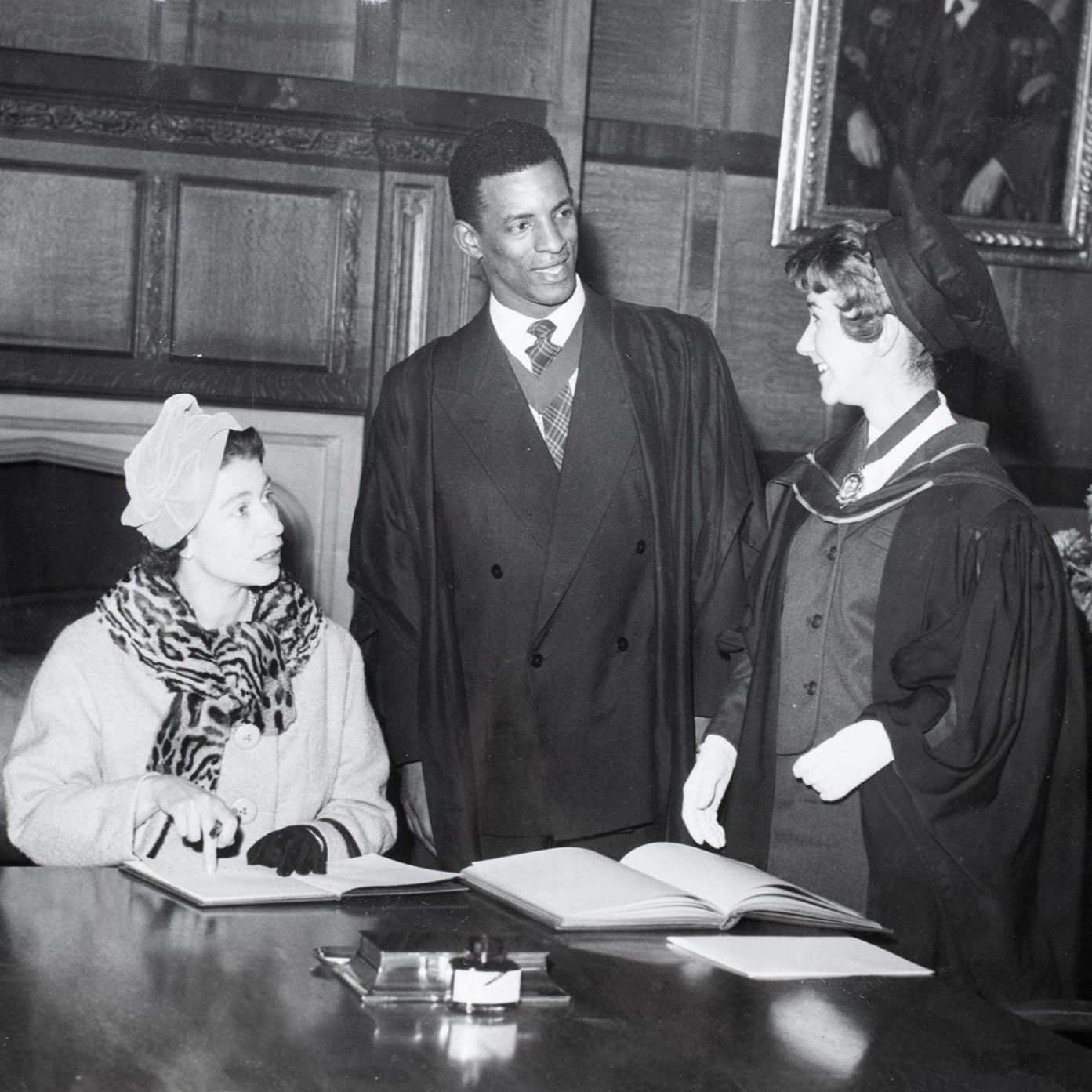 George Odlum stands at a table with Queen Elizabeth II seated at the table on a visit to the University of Bristol